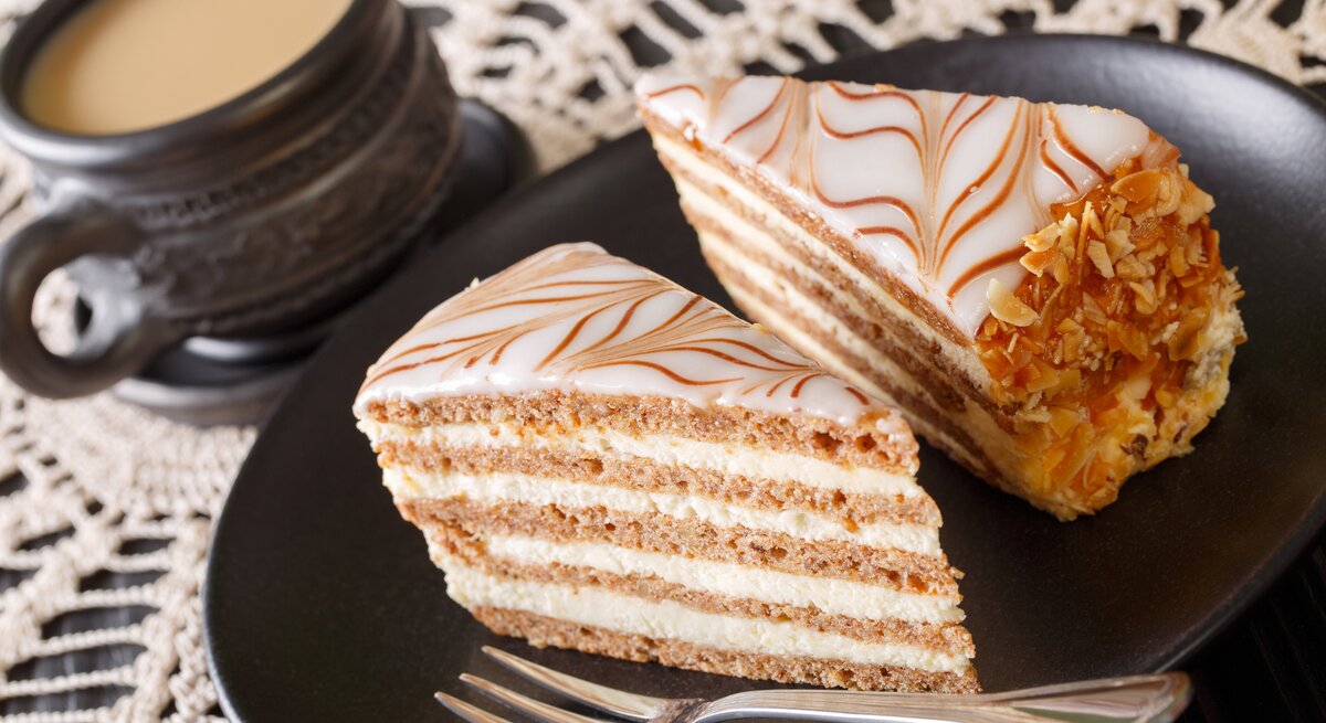 Geschichtete Buttercremetorte auf schwarzem Teller auf gehäkelter Tischdecke. 
