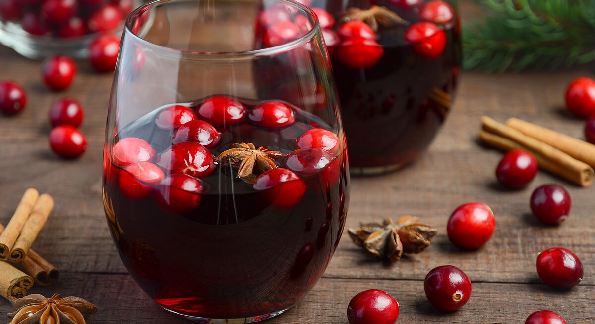 Ein Holztisch mit zwei Gläsern und Glühwein nah fotografiert. im Hintergrund Tannenzweige und Weihnachtsdeko.