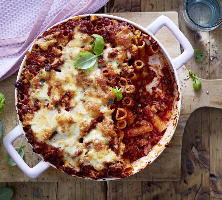 Rigatoni-Auflauf mit Hacksoße in einer weißen Auflaufform auf einem Holzbrett. | © EAT CLUB/Isabell Triemer