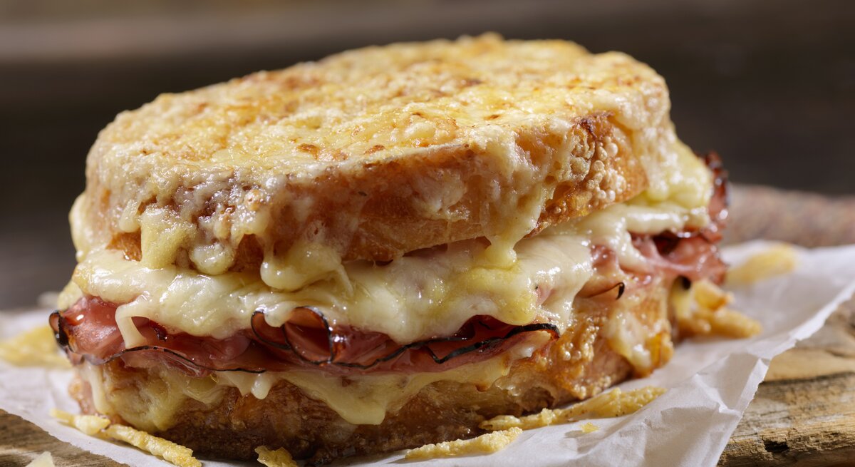 Seitliche Ansicht eines mit Käse überbackenen Croque Monsieur.