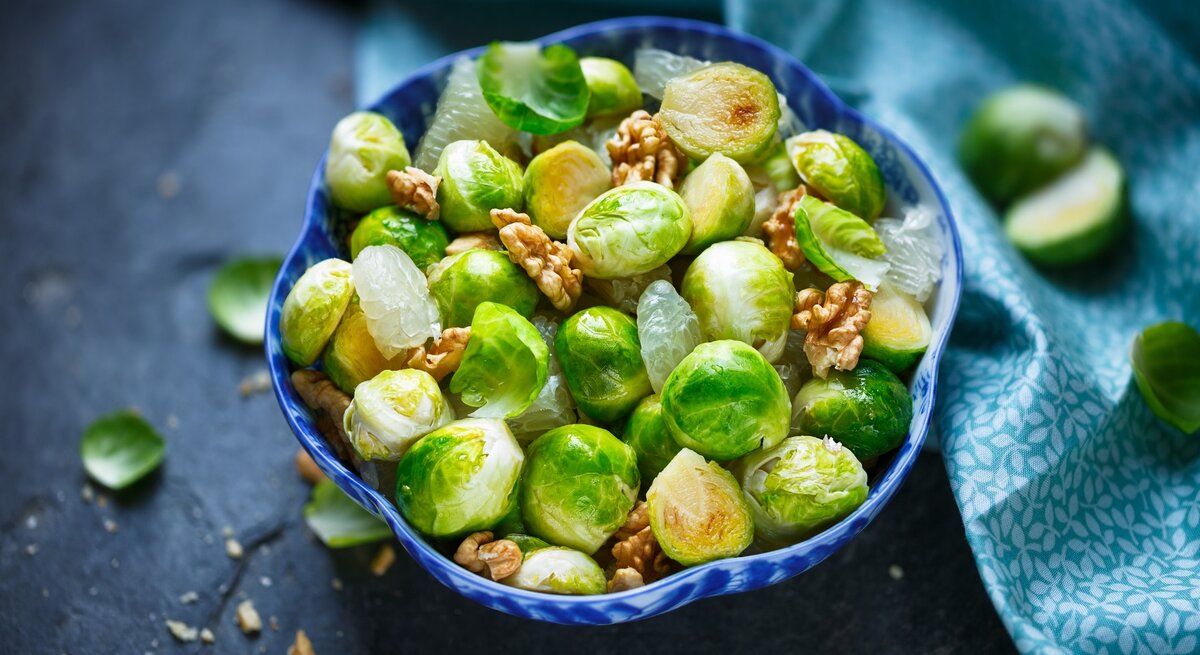 Gerösteter Rosenkohlsalat mit Walnuss, Pomelo und Honig-Dressing in blauer Schüssel auf blauem Untergrund. Draufsicht.