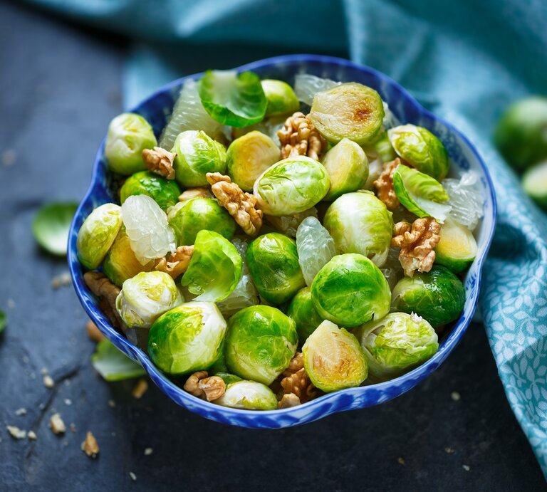 Gerösteter Rosenkohlsalat mit Walnuss, Pomelo und Honig-Dressing in blauer Schüssel auf blauem Untergrund. Draufsicht. | © Getty Images / asab974