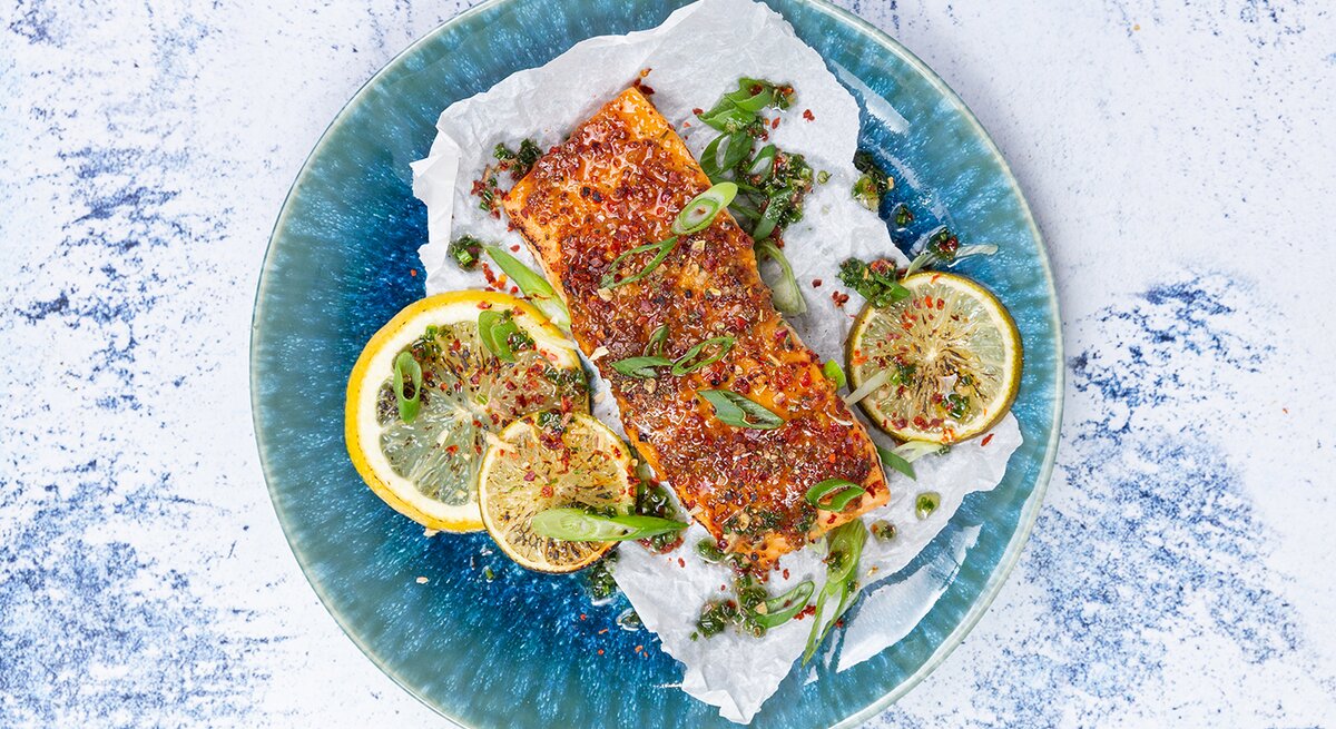 Karamellisierter Lachs mit Koblauchreis auf einem blauen Teller auf weiß-blauem Hintergrund.