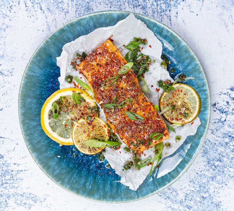 Karamellisierter Lachs mit Koblauchreis auf einem blauen Teller auf weiß-blauem Hintergrund. | © Just Spices
