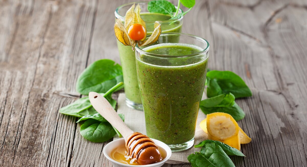 zwei Gläser gefüllt mit einem dickflüssigen, grünen Smoothie auf Holz. 