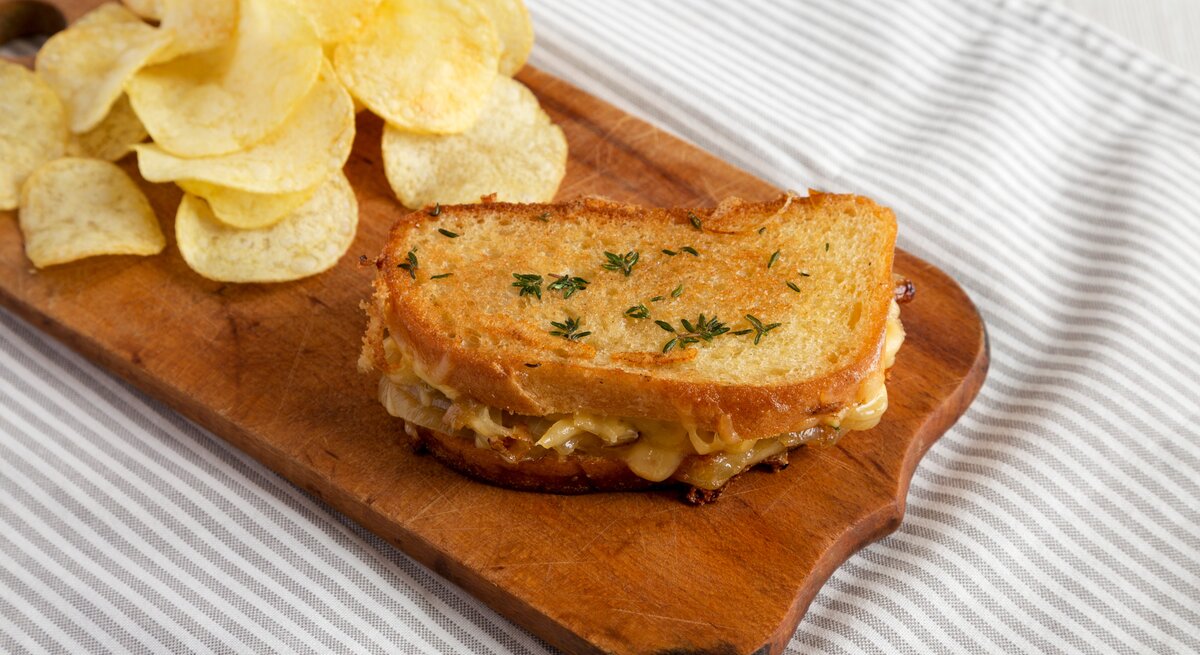 Französisches Käsesandwich mit geschmelzten Zwiebeln und Chips auf Holzplatte auf Tuch. Draufsicht.