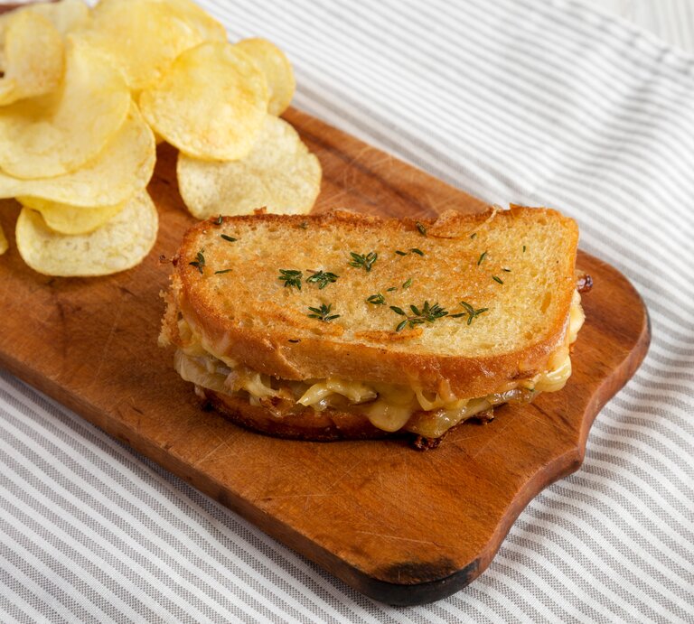 Französisches Käsesandwich mit geschmelzten Zwiebeln und Chips auf Holzplatte auf Tuch. Draufsicht. | © Shutterstock / Liudmyla Chuhunova