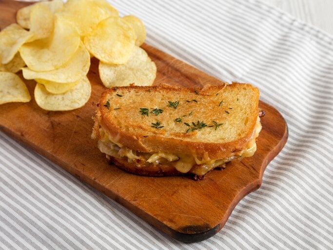 Französisches Käsesandwich mit geschmelzten Zwiebeln und Chips auf Holzplatte auf Tuch. Draufsicht. | © Shutterstock / Liudmyla Chuhunova