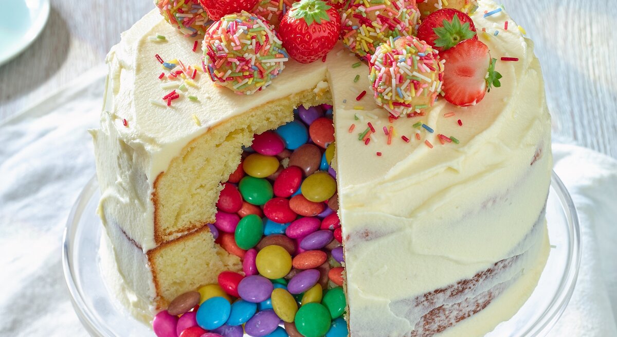 Piñata-Torte mit Erdbeeren auf einem Tortenteller vor weißem Hintergrund. 