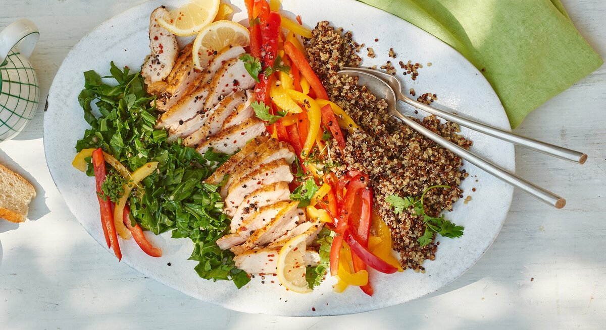 Quinoa-Hähnchen-Salat mit Rucola auf einem weißen Teller vor hellem Hintergrund, darauf ein grünes Tuch.