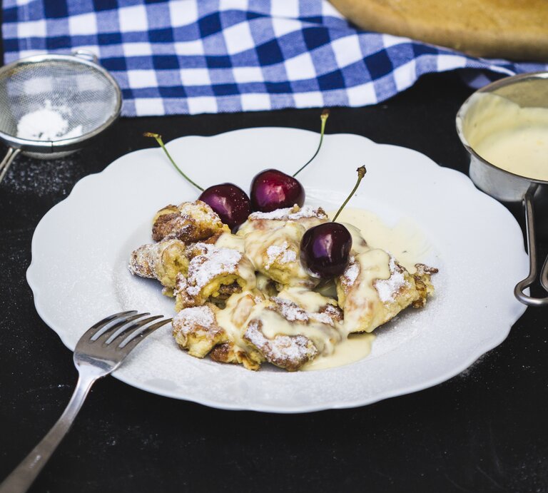 Kaiserschmarrn mit Kirschen und Vanillesauce aus einem runden Teller / Sieb mit Puderzucker / Draufsicht, schräg | © StockFood / Kurz, Antonia