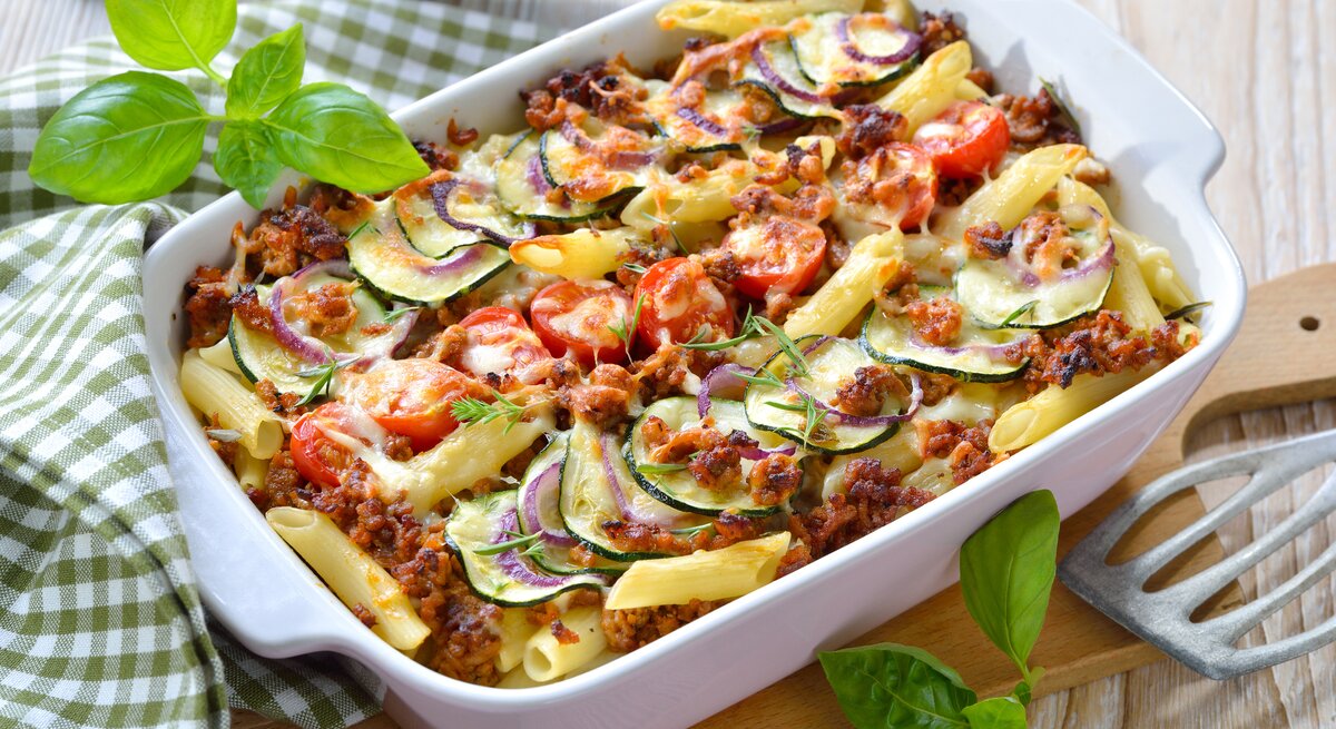 Weiße Auflaufform gefüllt mit traditioneller Penne al forno – lecker mit Hack und Zucchini!