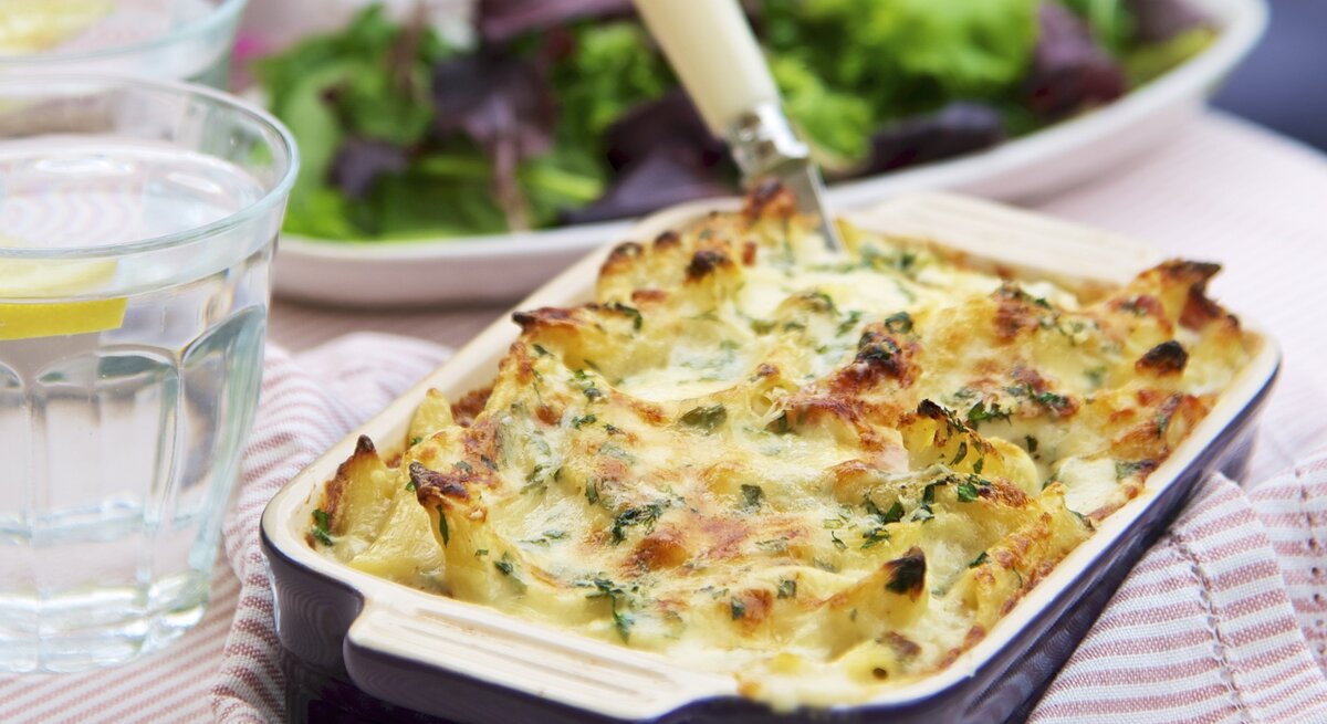 Nudel-Schinken-Auflauf in einer Form / Hintergrund grüner Salat / 