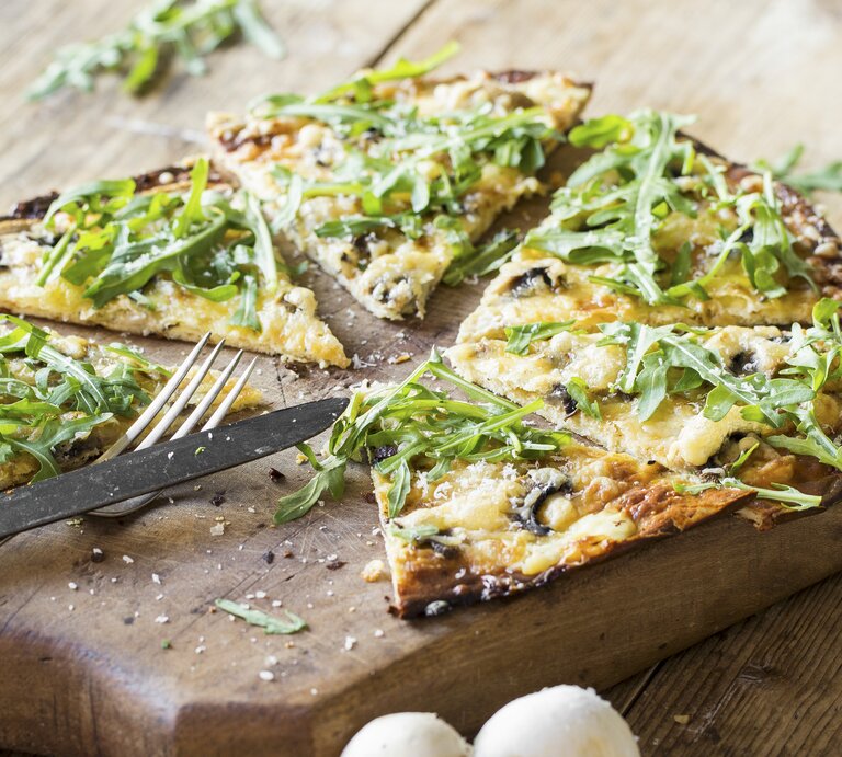 Nahaufnahme vom in Stücke geschnittenen, veganen Flammkuchen mit Rucola und Pilzen. | © StockFood/Springlane