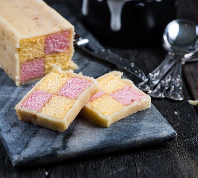 Angeschnittener britischer Battenburg-Kuchen auf einer dunklen Steinplatte auf einem dunklen Holztisch. | © GettyImages/ merc67