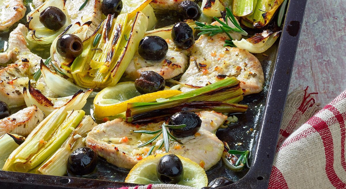 Zarte Hähnchenfilets mit schwarzen Oliven, Lauch, Fenchel, Zitrone und Rosmarin auf einem Blech goldbraun gebacken.