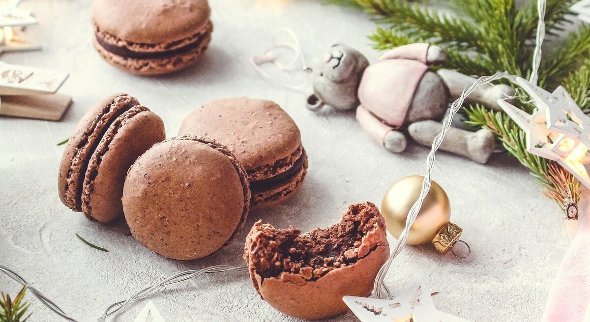 Weihnachtliche Schokoladen-Macarons mit Haselnüssen und Tonkabohne auf einem grauen Tisch mit weihnachtlicher Deko.