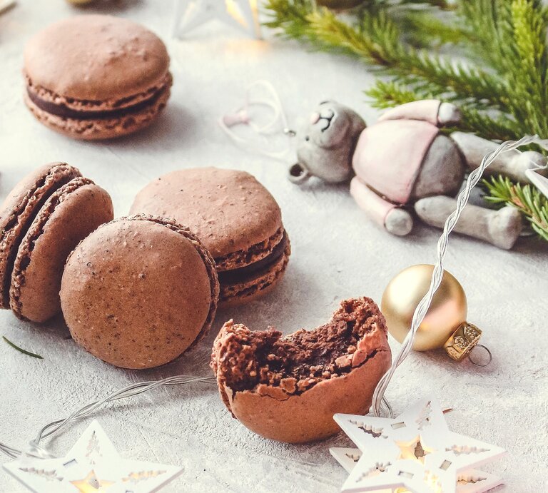 Weihnachtliche Schokoladen-Macarons mit Haselnüssen und Tonkabohne auf einem grauen Tisch mit weihnachtlicher Deko. | © StockFood / PhotoCuisine