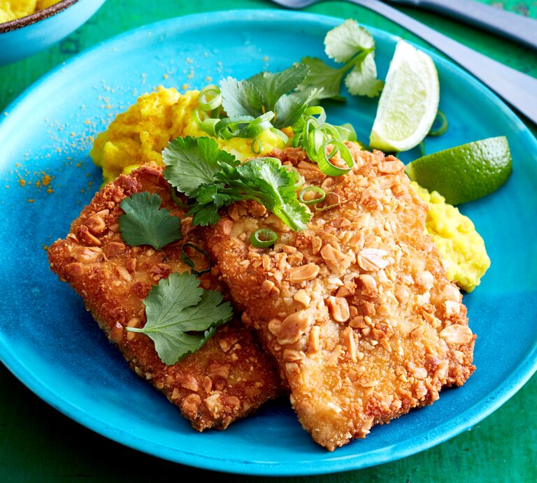 Erdnuss-Schnitzel mit Curry-Stampf auf einem Teller serviert. Rechts davon Besteck. Draufsicht. | © Eat Club; Isabell Triemer