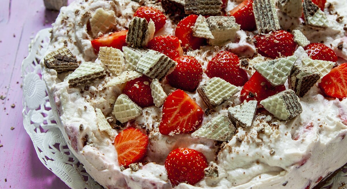 Die Erdbeer-Manner-Torte auf einem violetten Holztisch von schräg oben fotografiert.