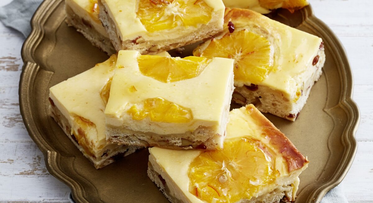 Orangen-Käseschnitten mit Stollenboden auf einem goldenen Teller auf hellem Hintergrund.