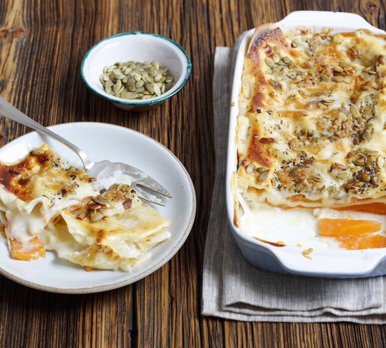 Die vegetarische Kürbis-Lasagne mit Kürbiskernen auf einem dunklen Holztisch von schräg oben fotografiert. | © StockFood / Castilho, Rua