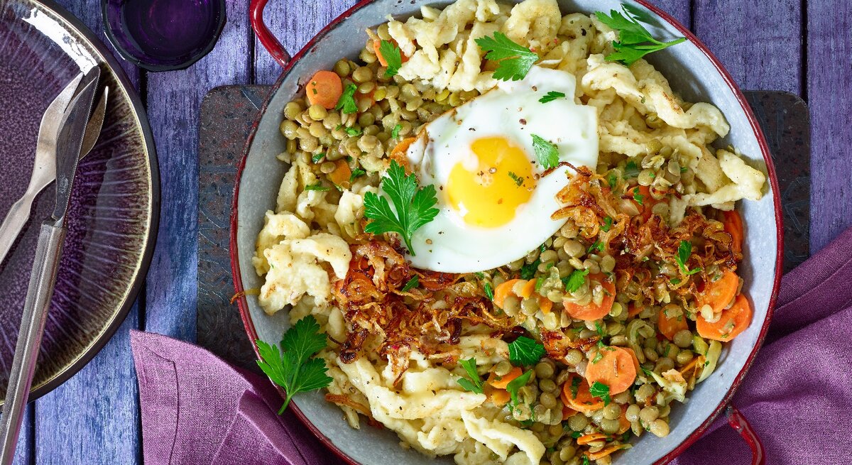 Spätzle-Linsenpfanne mit Spiegeleiern in einer Pfanne auf hölzernem Hintergrund. 