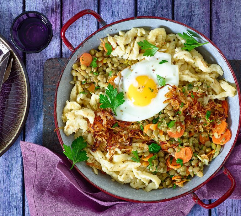Spätzle-Linsenpfanne mit Spiegeleiern in einer Pfanne auf hölzernem Hintergrund.  | © Matthias Liebich