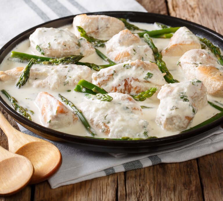 Gusseiserne Pfanne mit Hähnchen in Spargel-Sahnsesoße auf hölzernem Untergrund.  | © Getty Images/ALLEKO