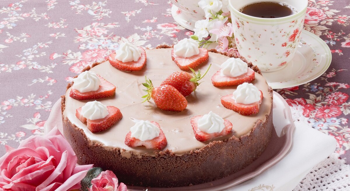 Die Torte auf einem Tisch mit Blumentischdecke. Alles von schräg oben fotografiert.