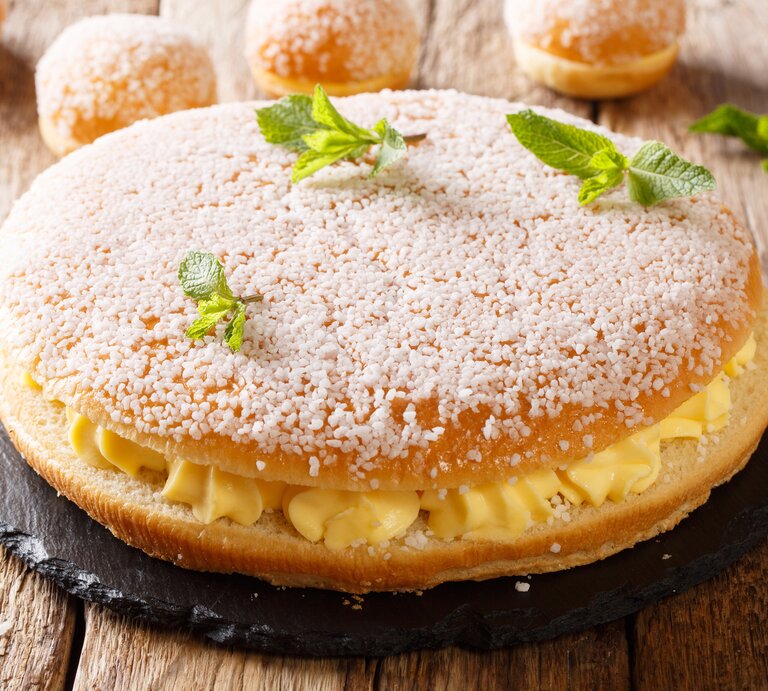 Kuchen mit Hagelzucker und Cremefüllung auf hölzernem Untergrund.  | © Getty images/ALLEKO