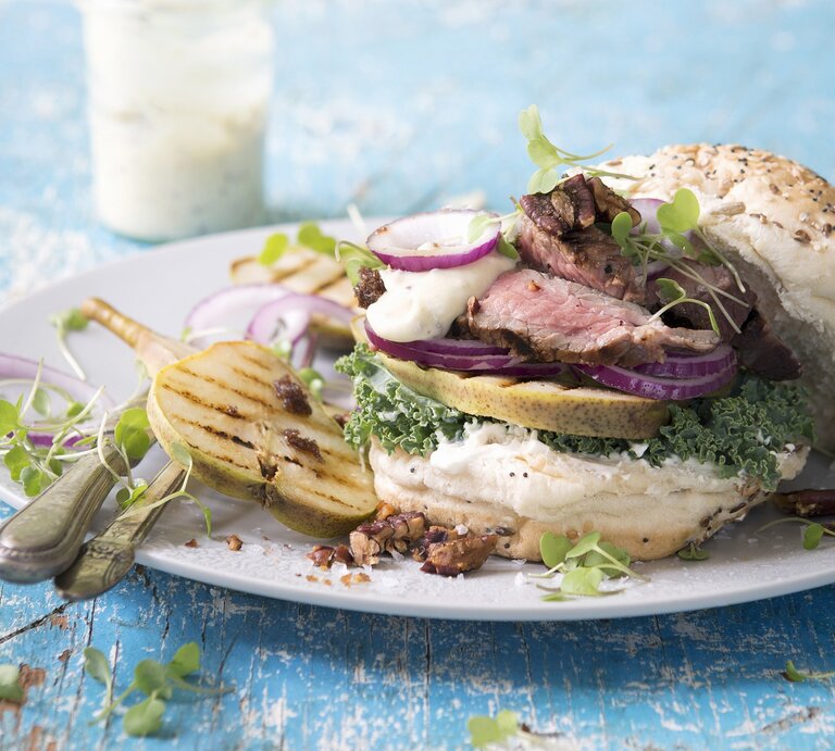 Der Burger auf einem weißen Teller mit hellblauem Tisch von der Seite fotografiert. | © StockFood / Great Stock!
