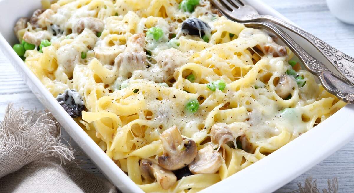 Ein Auflaufgericht mit cremigen Bandnudeln, gemischt mit grünen Erbsen und geschnittenen Champignons, großzügig überzogen mit geschmolzenem Käse. 