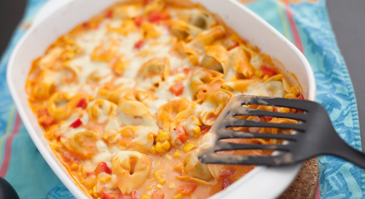 Weiße Auflaufform gefüllt mit Tortellini, Mais und cremiger Tomatensoße. 