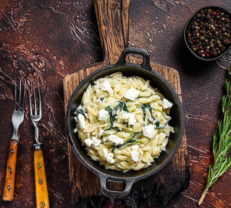 Gusseiserne Pfanne gefüllt mit Nudelreis, Spinat und Käse in rustikalem Ambiente mit mediterraner Dekoration. | © Getty Images/ Vladimir Mironov