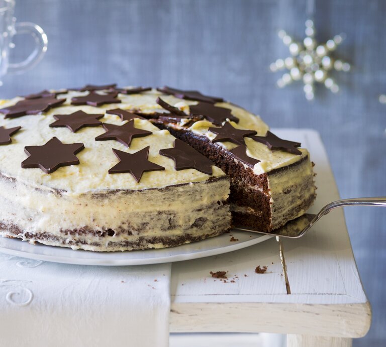 Weißer Kuchen mit schokoladigen Sternen vor weihnachtlich geschmücktem, blauen Hintergrund.  | © Stockfood/Jörn Rynio