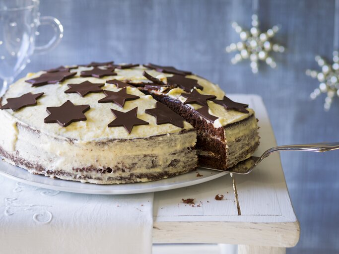 Weißer Kuchen mit schokoladigen Sternen vor weihnachtlich geschmücktem, blauen Hintergrund.  | © Stockfood/Jörn Rynio