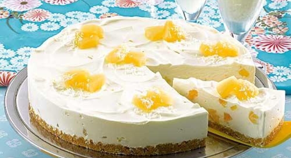 Pina-Colada-Torte mit Ananas-Stücken / Angeschnitten / 1 Stück Torte auf Tortenheber /  Zwei gefüllte Cocktailgläser / Untergrund Tisch / Draufsicht schäg
