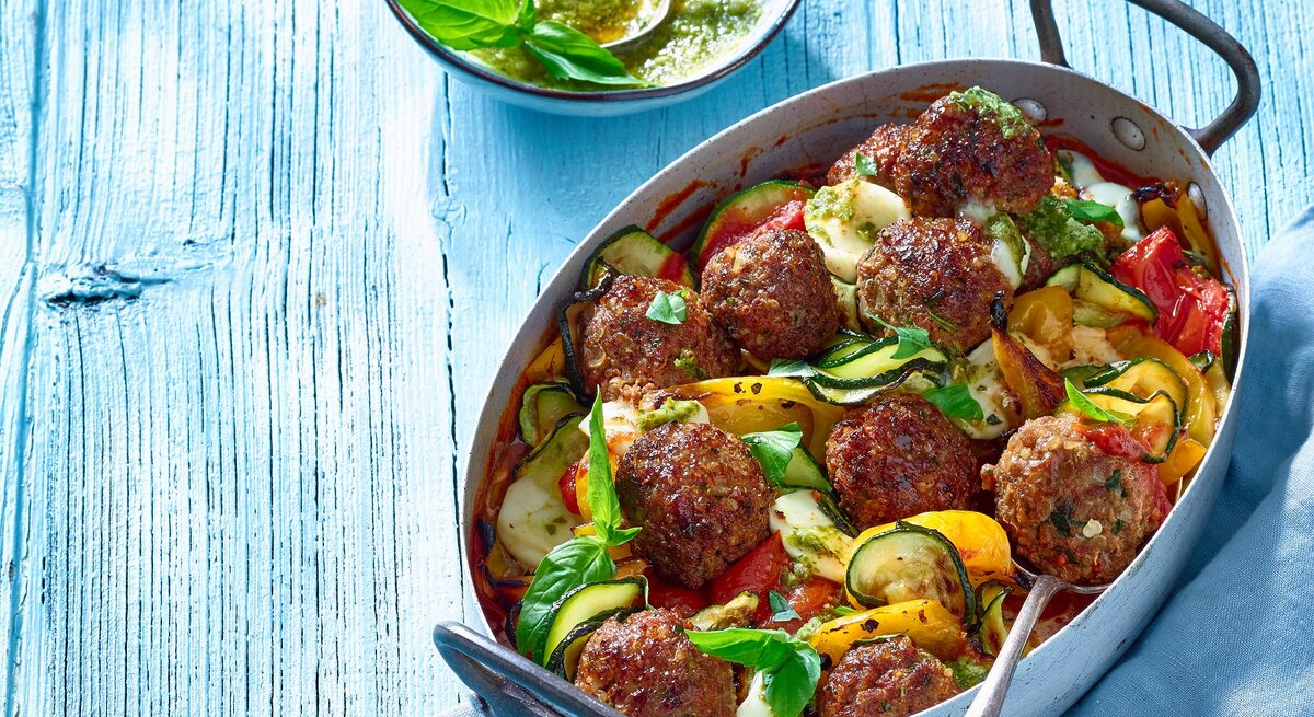 Draufsicht: ein Ratatouille-Hackbällchen-Pfanne in einer Form. Daneben eine runde Schale mit einer Sauce.
