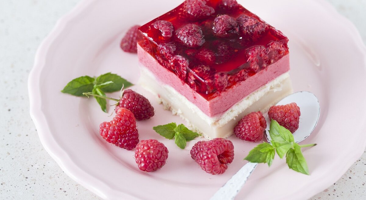 Ein Stück vom Himbeerkuchen auf einem hellen Teller weißem Untergrund.