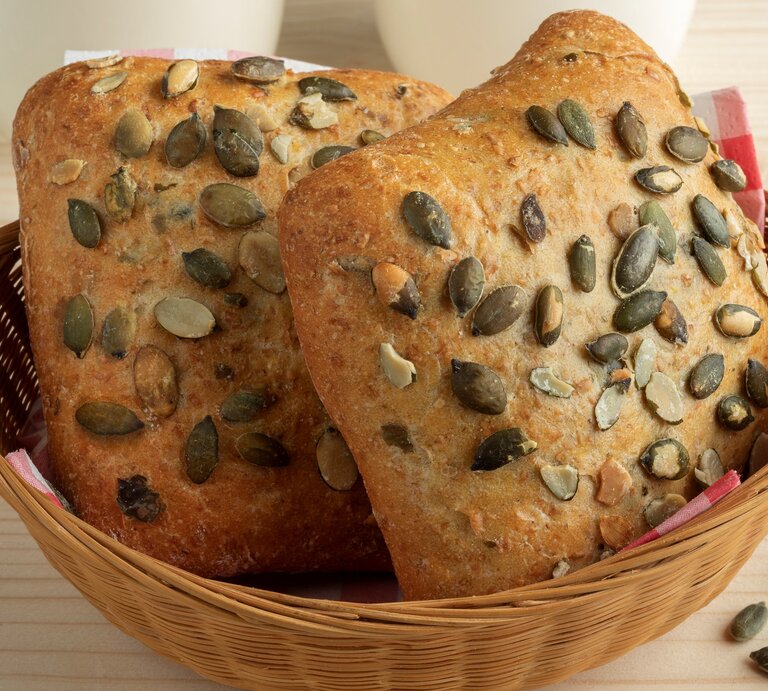Selbst gemachte Kürbiskernbrötchen in Brotkorb auf Holztisch. Im Bild zwei weiße Tassen und einige Kürbiskerne. Frontalansicht. | © Getty Images / PicturePartners