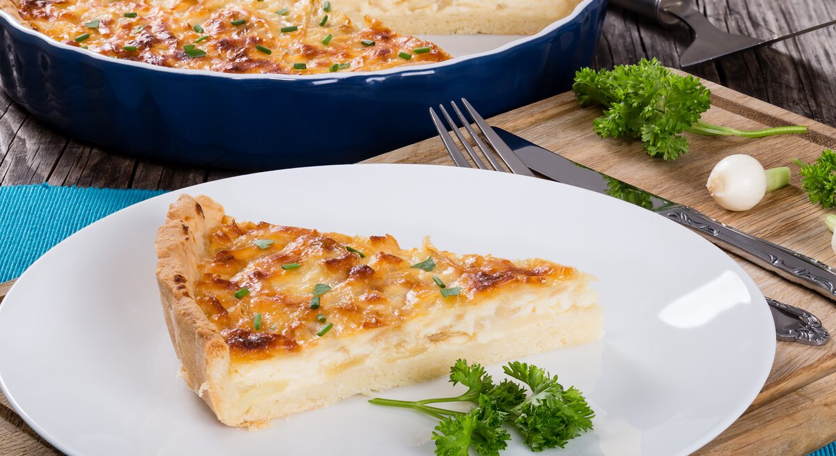 Ein Stück Käse-Quiche auf Teller in rustikalem Ambiente.