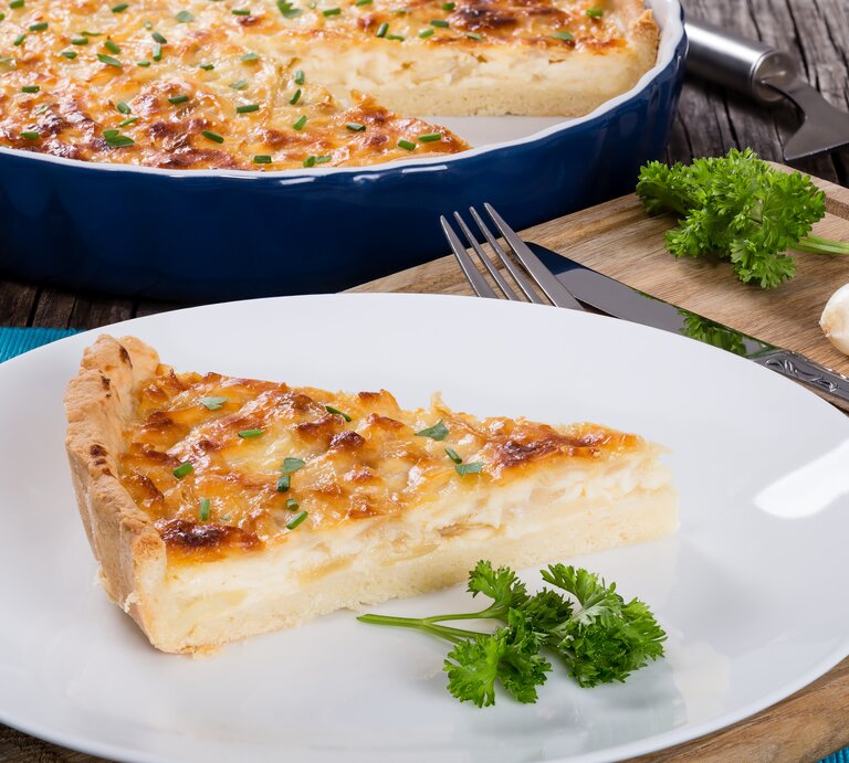 Ein Stück Käse-Quiche auf Teller in rustikalem Ambiente. | © GettyImages/from_my_point_of_view