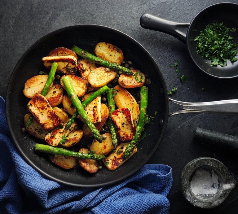 Spargel-Halloumi-Pfanne mit Kartoffeln in gusseiserner Pfanne auf dunklem Untergrund.  | © Getty Images/ haoliang