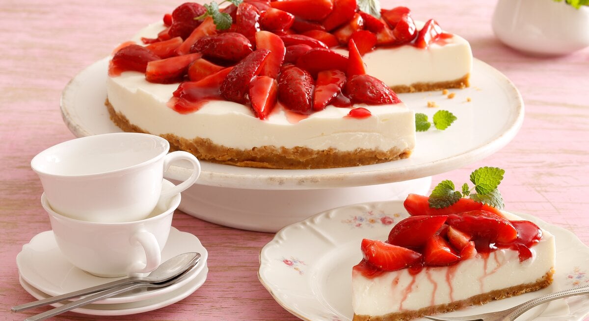 Die Erdbeer-Joghurttorte auf einem rosafarbenen Tisch von schräg oben fotografiert.