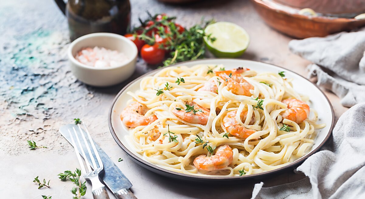 Ein Teller mit frisch zubereiteten Pasta, garniert mit saftigen, rosa Garnelen und fein gehackten Kräutern, serviert auf einem rustikalen Küchentisch.