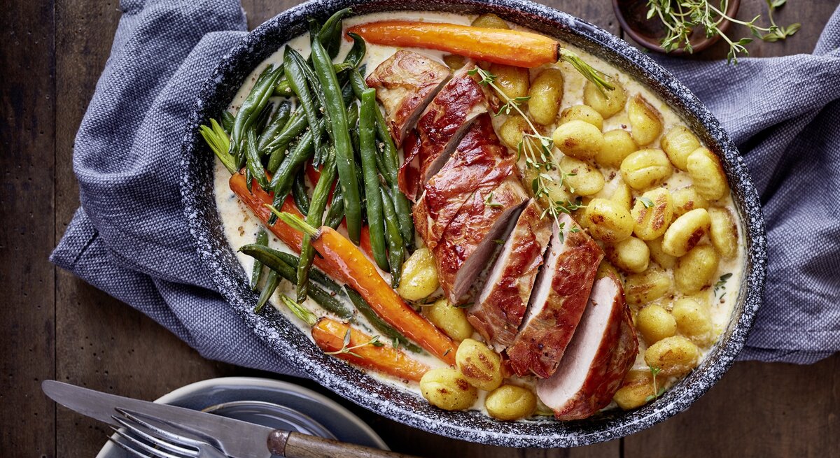 In Rahmsoße gebackenes Schweinefilet mit Gnocchi, glasierten Möhren und grünen Bohnen in rustikaler Auflaufform.