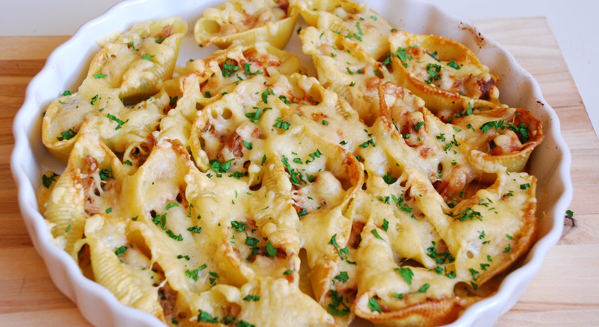 Muschel-Nudeln mit Thunfisch überbacken in weißer Auflaufform auf hölzernem Untergrund. 