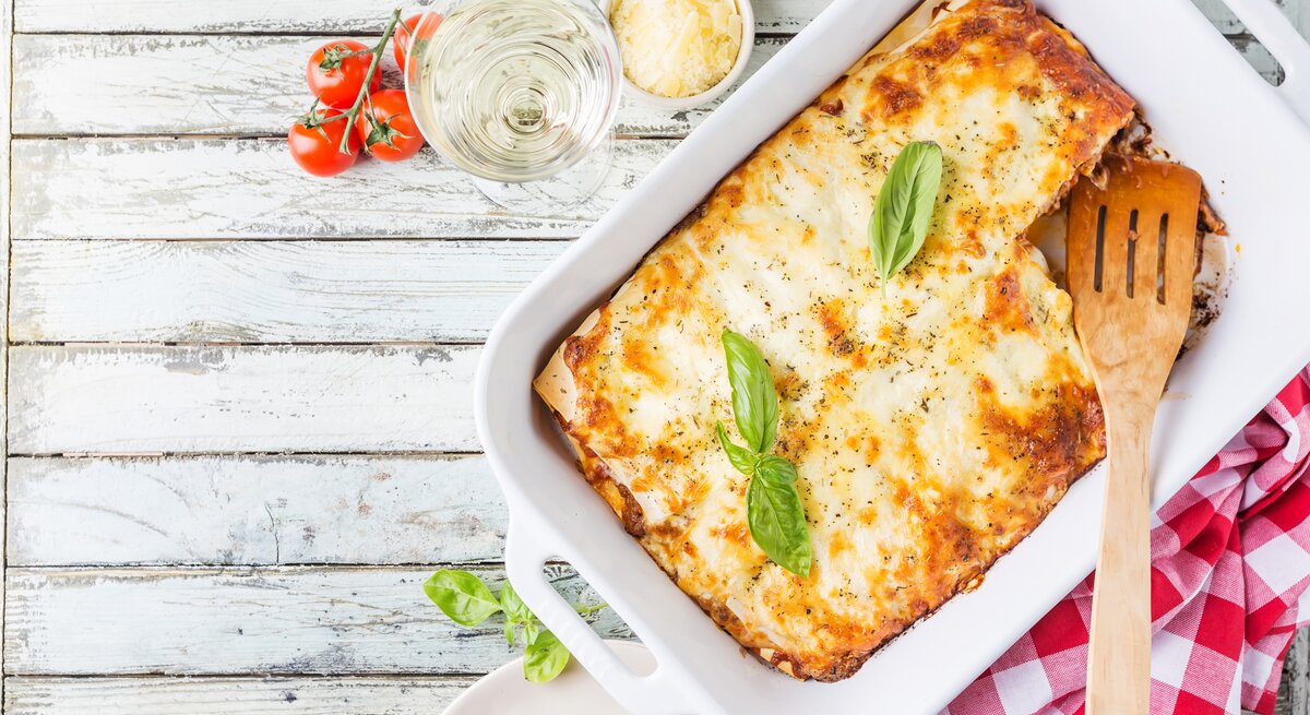 Die Lasagne auf einem hellen Holztisch von oben in der Auflaufform fotografiert.