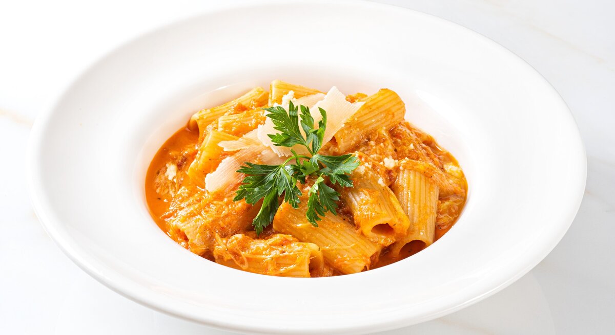 Pasta in Creme-fraiche-Soße in weißem Teller auf weißem Untergrund mit Petersilie. Draufsicht.